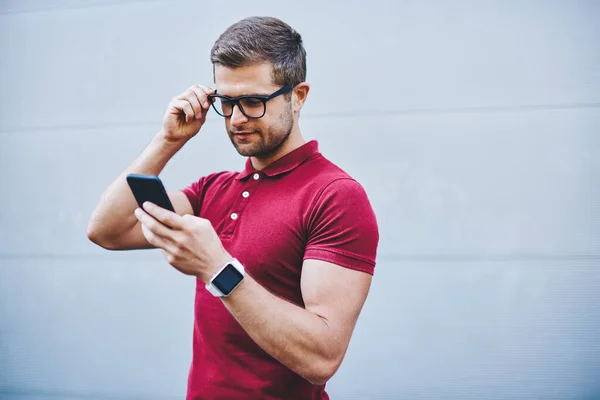 Thoughtful Man Beard Trendy Outfit Wristwatch Touching Eyeglasses Browsing Smartphone — Stock Photo, Image
