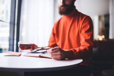 Düşük açılı günlük giysiler içinde bir bardak çay ve gözlüklü bir adam boş vakitlerinde masada oturuyor.