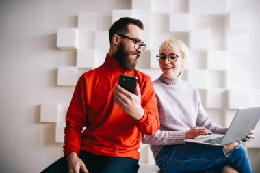 Gündelik giysiler içinde gülümseyen bir adam hafif iş yerinde birlikte çalışırken akıllı telefon ekranını kadın iş arkadaşıyla paylaşıyor.