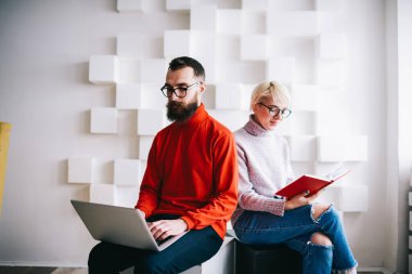 Dizüstü bilgisayarda çalışan sakallı bir erkek ve kadın serbest çalışan, gündelik kıyafetlerle notlarda notlar okuyan, açık modern işyerinde vakit geçiren biri.