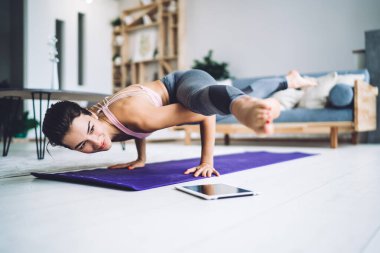 Sıradan sportif giyinen güçlü bir kadın Asya 'da, halının üzerinde duruyor kaslarını esnetiyor, formda bir kız, modern ev içlerinde esneklik eğitimi almak için sabah yogasının keyfini çıkarıyor.