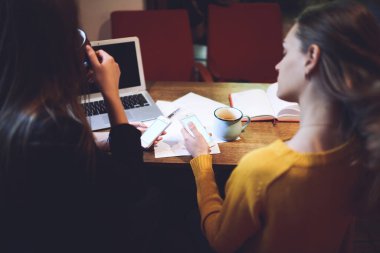 Uzaktan kumandalı kadın çalışanlar kahve fincanları ve dizüstü bilgisayarlarla birlikte akıllı telefonlarda sörf yapıyorlar.