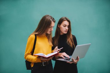 Modern dizüstü bilgisayar ve cep telefonu kullanarak yeni proje için bilgi toplayan ve birlikte eğitim gören düşünceli bayan öğrenciler.