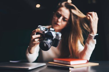 Eski model fotoğraf makinesinin seçici odağı genç bir kadının elinde dizüstü bilgisayar ve kitaplarla gündüz vakti masada oturması.