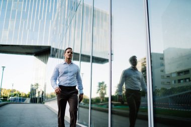 Beyaz bir sahibi, 30 yaşında, iş molasında cam ofis binasının yanında yürüyor. Şehir merkezindeki iş toplantısına giden zeki bir erkek girişimci.