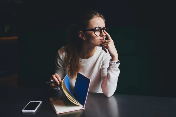 若い女性のフリーランスは 時間の経過とともに仕事中にノートブックのページを反転メガネに触れる携帯電話でテーブルに座って見て — ストック写真