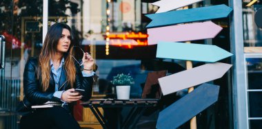 Genç düşünceli kız öğrenci ara verdiğinde elinde gözlük, elinde gözlüklerle kafeteryada oturuyor.