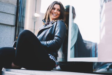 Genç ve şık bir bayanın gündelik kıyafetleri içinde pencerenin yanındaki caddeye bakıyor ve güzel bir hava var.