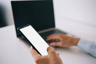 Modern ofiste dizüstü bilgisayarla yazı yazarken resmi tişörtlü, tanınmayan bir erkek müdürün cep telefonundan.