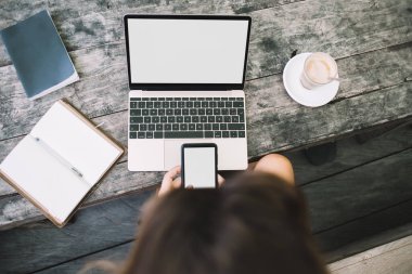 Bilgisayar kullanan, elinde not defteri ve kahveyle masada oturan, akıllı telefonlu tanınmayan bir kadın serbest yazar.