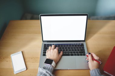 Yukarıdan gelen, süveter ve akıllı kadın, ahşap masada akıllı telefon ve kalemle otururken boş ekranlı modern netbook kullanıyor.