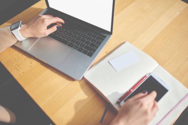 Yukardan gelen yüzü olmayan, akıllı giyinen, modern netbook üzerinde çalışan, akıllı telefonlu ve açık defterli bir kadın.