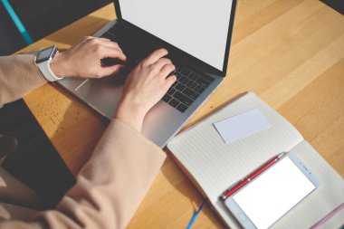 Yukardan gelen, sıradan kıyafetlerle tanınmayan bir kadın, ahşap masada akıllı telefon ve günlükle otururken boş ekran ile modern netbook 'a göz atıyor.