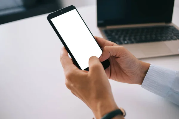オフィスでプロジェクトに取り組んでいる間 スマートフォンを空の画面で閲覧し ラップトップでテーブルに座ってシャツの顔のない人をトリミング — ストック写真