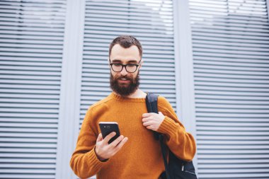 Düşük açılı neşeli erkek cep telefonu ekranına bakıyor mesajları kontrol ediyor ve boş zamanlarını sokakta yürüyor.