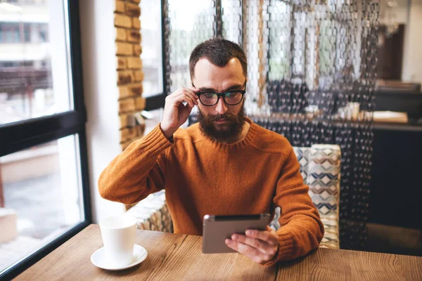 Concentrated Bearded Male Sitting Table Cup Coffee Touching Eyeglasses Looking — Stockfoto