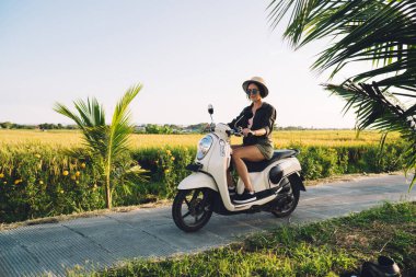 Çekici beyaz turistin eski moda scooter sürüşünü doğa ortamında güneşli havanın tadını çıkarışını, güzel hippi kızın yolculuk sırasında klasik motosikleti test edişini.