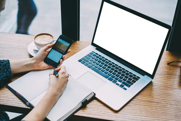 Masada dizüstü bilgisayarla oturan, akıllı telefondan resim izleyen ve çalışırken not alan ekinsiz insanlardan.