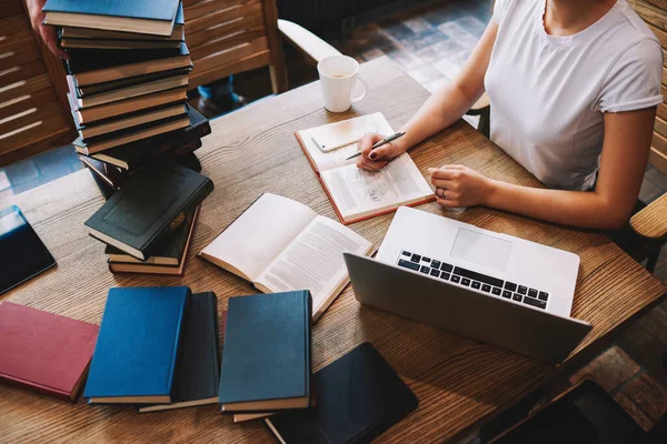 Diz üstü bilgisayarı ve kütüphanede okurken bir sürü kitapla ahşap masada oturan yüzü olmayan kız öğrencilerden.