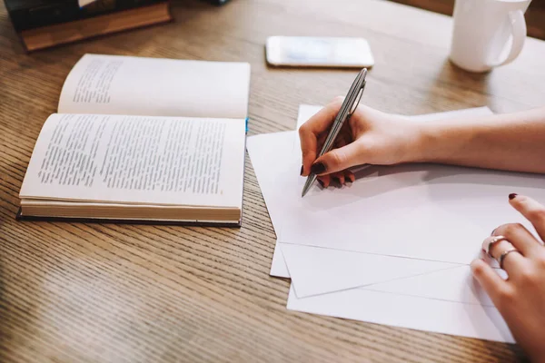 Kırpılmış yüzü olmayan bir kadın açık bir kitapla masada oturuyor ve sınava hazırlanırken notlar alıyor.