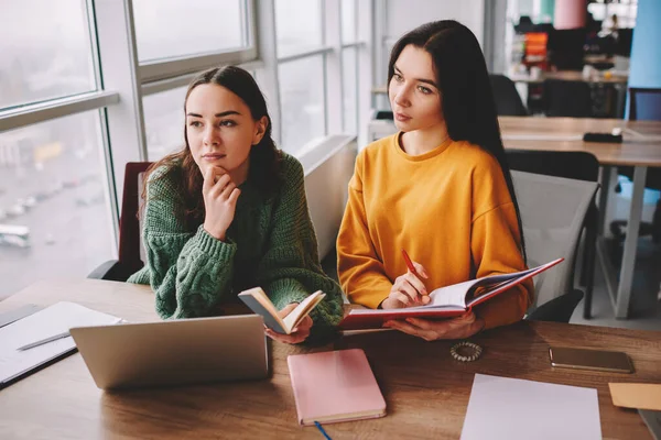 Young Thoughtful Female Students Looking Away Sitting Wooden Table Notebooks — Stock Photo, Image