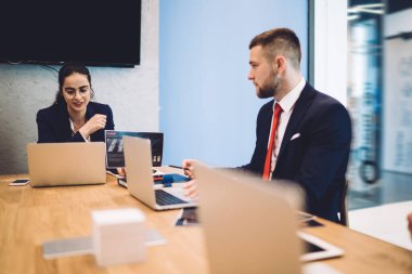 Resmi olarak düşünceli bir iş adamı dizüstü bilgisayarla masaya oturur ve modern ofisteki bayan meslektaşıyla proje sonuçlarını tartışır.