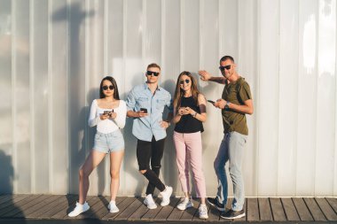 Moda kıyafetleri giymiş hippi erkeklerin reklam alanında poz verdirdikleri uzun bir portre. 20 'li yaşlarda genç erkek ve kadın en iyi arkadaşlar şehirde boş zamanlarında akıllı telefon kullanıyorlar.