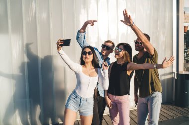 Şehirdeki dostça buluşmalar sırasında video blogu çeken Kafkasyalı genç nüfuzlu blogcular, modern akıllı telefon aygıtı kullanarak selfie çekimleri için poz veren genç erkek ve kadın hipsterler.