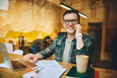 Her ne kadar kameraya bakan serbest gülümseyen erkek bir cam olsa da ahşap masada oturmuş laptopu iş için kullanıyor kafede cep telefonuyla sohbet ediyor.