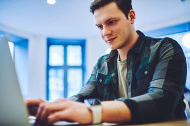 Modern ferah iş yerinde yeni bir proje üzerinde çalışmak için dizüstü bilgisayar kullanan, günlük kıyafetleri olan, ekin odaklı bir adamdan.