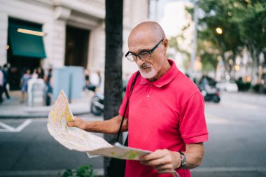 Gözlüklü, sıradan giyinmiş, yaşlı, sakallı ve kel bir adam. Yalnız seyahat ediyor ve yabancı bir şehri gezmek için haritada yürüyor.