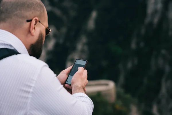 サンタ マリア モンセラット修道院で時間を過ごしながら ソーシャルメディアをチェックするための携帯電話をサーフィン眼鏡で上記の作物の男からのバックビュー — ストック写真