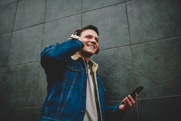 Yüzünde dişlek bir gülümseme olan, duvarın yanından uzaklaşan, kulaklıkla müzik dinleyen ve akıllı telefonları karıştıran pozitif bir erkekten.