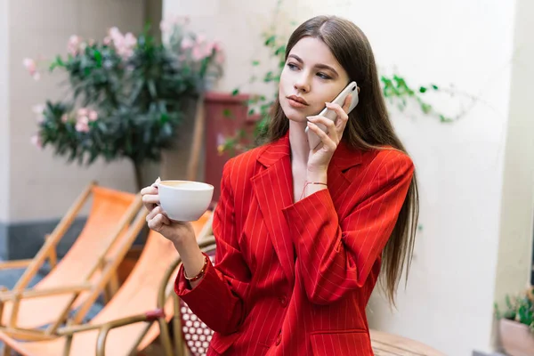 Задумчивая Молодая Женщина Модной Одежде Разговаривает Мобильному Телефону Стоя Чашкой — стоковое фото