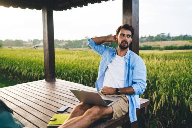 Tarz sahibi, genç, sakallı iş adamı. Günlük giysiler içinde, netbook projesinde çalışıyor. Kırsal kesimde yaz tatilleri boyunca ahşap köşkte oturuyor.