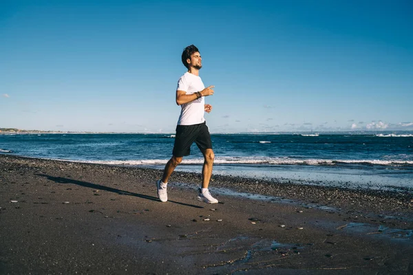 快適なスポーツウェアを身に着け 夏の晴れた日には波を振って近くの空のビーチで静かにジョギングするスポーツマン — ストック写真