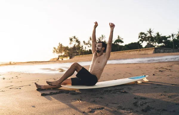 年轻的裸男冲浪手 穿着黑色短裤 鼻子和脸颊涂满厚厚的防晒霜 坐在沙滩上 在阳光下伸展着冲浪 — 图库照片