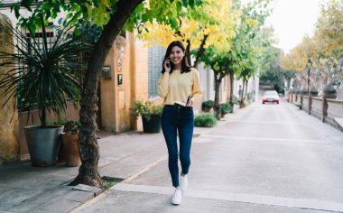 Elinde ders kitabı olan neşeli hippi turistin tam boy portresi seyahat gezileri hakkında notlar almak için rehberlik ediyor, mutlu Asyalı kadın uluslararası hücre sohbetinden hoşlanıyor.