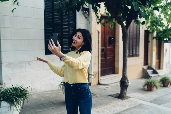 Elektronik kulaklıklardaki mutlu Asyalı video kaydedicisi cep telefonu kamerasıyla içeriği etkiliyor boş zamanlarında, neşeli hippi kız cep telefonuyla dolaşırken gülümsüyor.