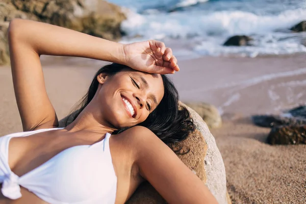 Bahamalar 'da bikini sezonunda kıyı taşında uzanmış güneşlenen neşeli bir kadın. Yüzünde mükemmel bir gülümsemeyle mutlu bir Latin kadın.