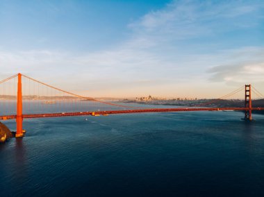 San Francisco 'nun sıcak bir gününde, ünlü şehirde bulunan mavi gökyüzüne karşı sakin okyanus üzerindeki Golden Gate köprüsünün insansız hava aracı görüntüsü.