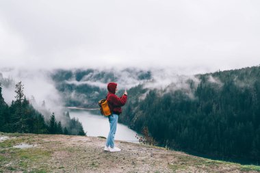 ABD 'de sonbahar günü sakin göl kenarındaki muhteşem dağların fotoğraflarını çeken isimsiz turistin yan görüntüsü