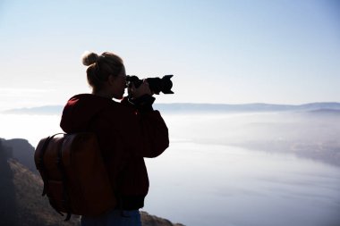 Amerika 'daki uçurumdan sisli bir nehirle fotoğraf makinesiyle muhteşem doğal manzaranın fotoğrafını çeken kadın turistin yan görüntüsü.