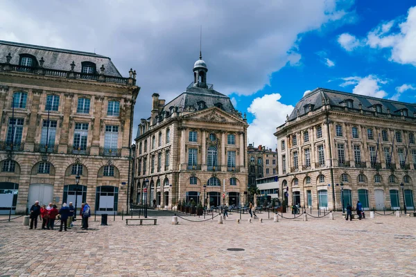 Bordeaux 'da bulutlu bir sonbahar gününde ortaçağ döneminden kalma tarihi binaların etrafında turistlerin dolaştığı eski asfalt bir meydan.