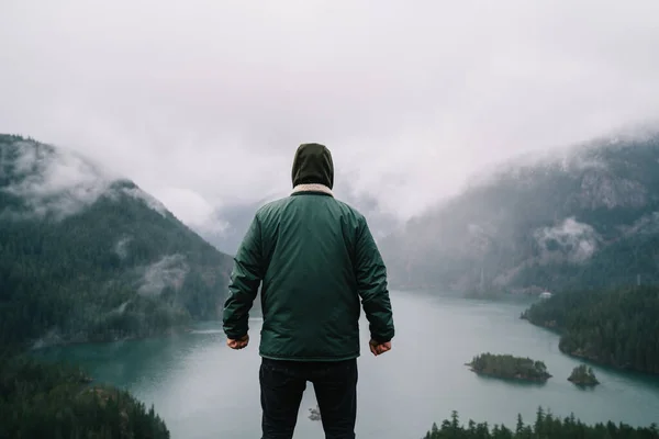 米国旅行中の風景美を楽しみながら 霧の中で曇り空の丘陵地帯で穏やかな湖の視点に立つアウターウェアの男性観光客のバックビュー — ストック写真