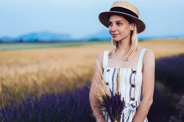 面带微笑的女性 头戴帽子 穿着衣服 站在薰衣草丛中 一边看着远方 一边在城外度暑假 — 图库照片