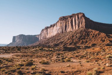 Heybetli dağların ve dikenli bitkilerin muhteşem manzarası Anıt Vadisi 'ndeki bulutsuz gökyüzünün arka planında kurak kırmızı kum çölüne yerleştirilmiş.
