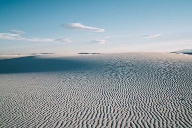 Beyaz Kumlar Ulusal Parkı 'nda güneşli bir günde çöldeki kumlu kumulların arasından mavi bulutlu gökyüzüne karşı