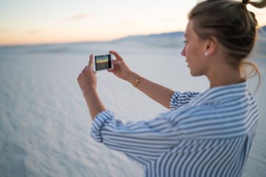 Beyaz Kumlar Ulusal Parkı 'nın ortasında duran ve fotoğraf çekerken ekran telefonuna odaklanan ekili kadın turist.