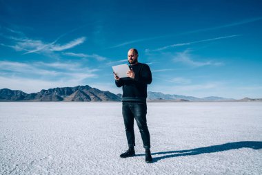 Modern tablet kullanarak ABD 'deki Utah tuz sahalarının doğal manzarasını keşfeden günlük giysiler içinde kel erkek turist.